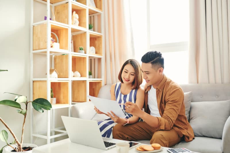 young asian couple sitting on a gray couch and looking at school options