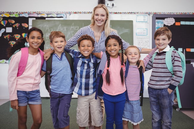 happy-teacher-standing-with-schoolkids-in-classroo-2021-08-28-17-58-12-utc