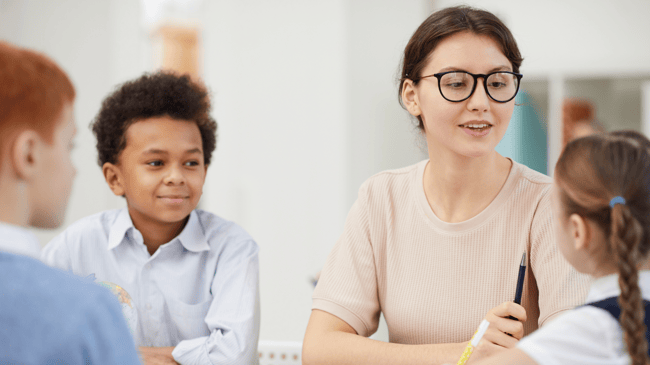 teacher sitting and talking to three young students at table