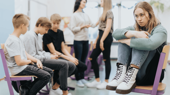 teenage high school girl sitting looking somber among classmates