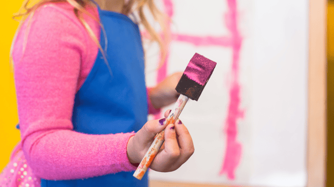 young girl handling pink paintbrush and painting