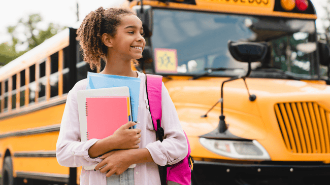 young girl standing outside bus with backpack