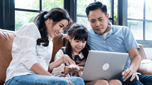 young parents with daughter sitting on couch and looking at a school website